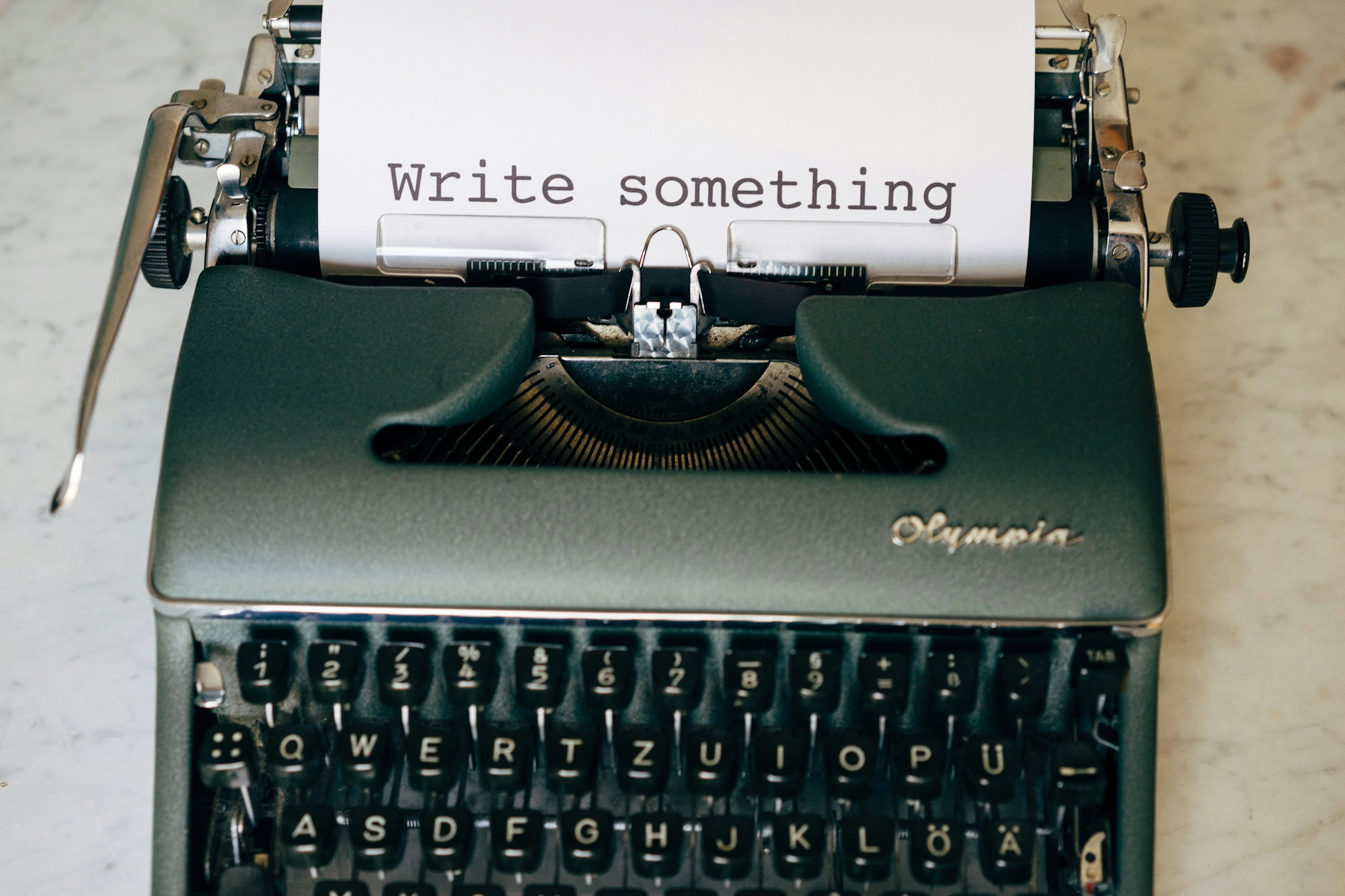 An Olympia typewriter with paper reading "Write something" on a marble surface